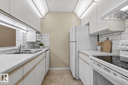 Galley kitchen featuring white cabinetry, subway tile backsplash, dual basin sink, and built-in white appliances - #102 6710 158 Av Nw, Edmonton, AB 
