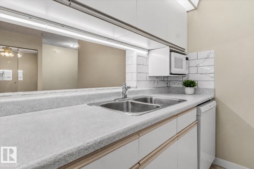 Compact kitchen space featuring a dual basin sink, white cabinetry with light wood-finish trim, and a built-in microwave - #102 6710 158 Av Nw, Edmonton, AB 