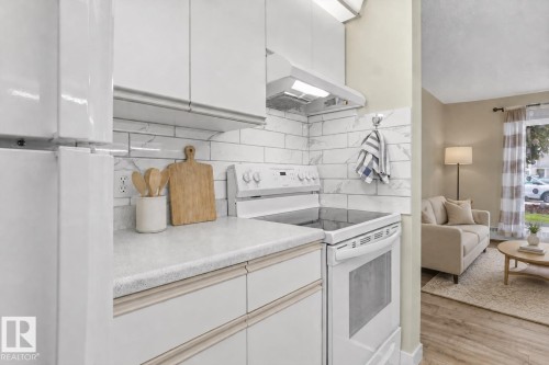 Kitchen featuring white cabinetry, light-toned countertops, subway tile backsplash, and a white electric range - #102 6710 158 Av Nw, Edmonton, AB 