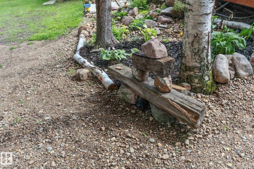 Gravel pathway with a landscaped garden bed featuring river rock edging, mature trees, and hosta plantings - 506 60017 Range Road 110 A, Rural St. Paul County, AB 