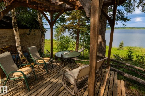 Wood-plank outdoor deck with partial pergola, surrounded by mature trees, overlooking a substantial body of water - 506 60017 Range Road 110 A, Rural St. Paul County, AB 