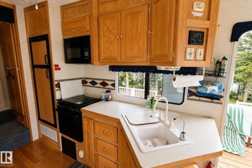 Compact kitchen featuring wood-finish cabinetry, a built-in microwave, a black range, and a dual-basin sink with a white countertop - 506 60017 Range Road 110 A, Rural St. Paul County, AB 