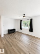 Spacious room featuring wood-finish flooring, a large window, a ceiling fan with integrated lighting, and white baseboards - 
