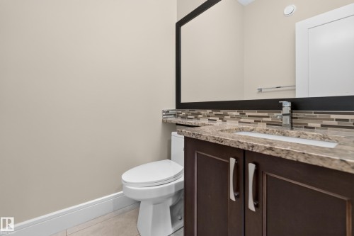 Dark wood-finish vanity with paneling, integrated sink, stone-finish countertop, and mosaic tile backsplash - 7014 Chivers Loop Sw, Edmonton, AB 