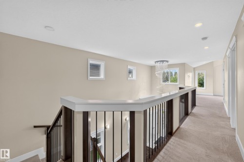 Upper-level hallway with neutral carpeting, recessed lighting, and a contemporary spiral chandelier - 7014 Chivers Loop Sw, Edmonton, AB 