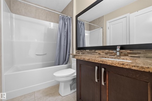 Integrated bathtub with a shower, dark wood-finish vanity with a light-colored countertop, and a full-width mirror - 7014 Chivers Loop Sw, Edmonton, AB 