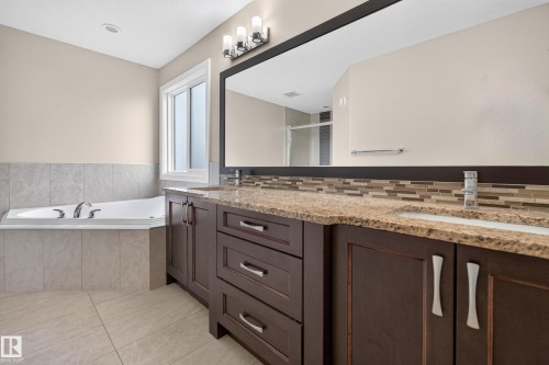 Dual vanity with granite countertops, tiled backsplash, large mirror, and dark wood-finish cabinetry - 7014 Chivers Loop Sw, Edmonton, AB 