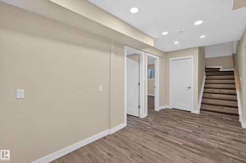 Recessed lighting illuminates the wood-finish flooring, staircase, and neutral-toned walls - 7014 Chivers Loop Sw, Edmonton, AB 