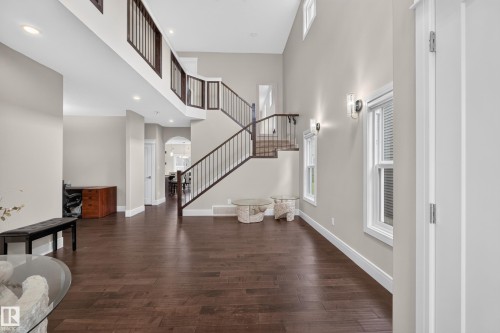 Two-story entry with hardwood flooring, a multi-level staircase featuring dark wood and metal railings, and natural light from tall windows - 7014 Chivers Loop Sw, Edmonton, AB 