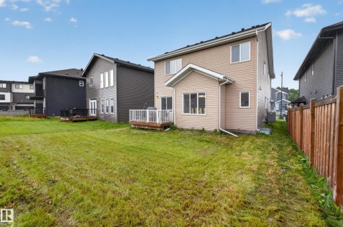 Expansive backyard with a manicured lawn, featuring a light tan siding exterior and an elevated deck with white railings - 7014 Chivers Loop Sw, Edmonton, AB 
