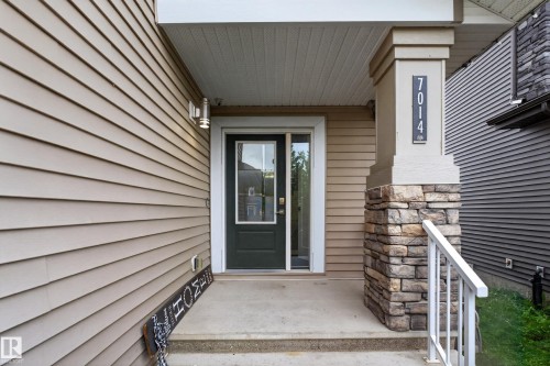 Concrete front porch featuring a dark entry door with glass paneling, stone pillar base, and vinyl siding - 7014 Chivers Loop Sw, Edmonton, AB 
