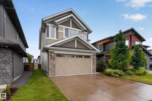 Two-story residence featuring a two-car garage with a paneled door, stone facade accents, and a concrete driveway - 7014 Chivers Loop Sw, Edmonton, AB 