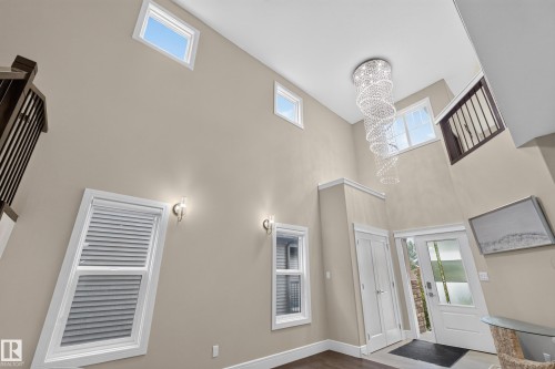 Soaring ceiling with multiple windows, crystal chandelier, and dark wood-finish flooring - 7014 Chivers Loop Sw, Edmonton, AB 