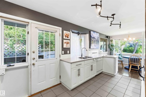 Kitchen featuring white cabinetry, light-toned countertops, a stainless-steel sink with a gooseneck faucet, and a dishwasher - 5208 105 Street Nw, Edmonton, AB - Indoor Photo Showing Kitchen With Double Sink