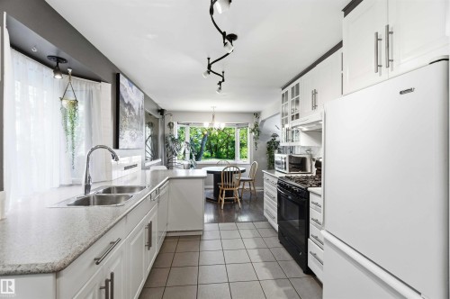 Galley kitchen featuring white cabinetry, light-toned countertops, and a double basin sink with a gooseneck faucet - 5208 105 Street Nw, Edmonton, AB - Indoor Photo Showing Kitchen With Double Sink