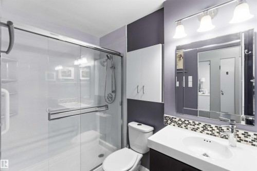 Bathroom featuring a glass-enclosed shower, white vanity with integrated sink, contemporary vanity mirror with sconce lighting, mosaic tile backsplash, and wall-mounted storage cabinetry - 5208 105 Street Nw, Edmonton, AB - Indoor Photo Showing Bathroom