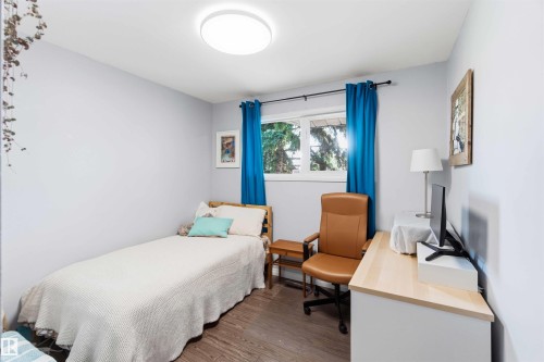 Bedroom with light gray walls, wood-finish flooring, a window with a black curtain rod, and a flush-mount ceiling light fixture - 5208 105 Street Nw, Edmonton, AB - Indoor Photo Showing Bedroom