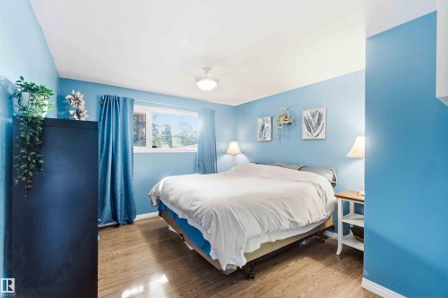 Spacious room featuring wood-finish flooring, light blue walls, and a large window with blue privacy drapes - 5208 105 Street Nw, Edmonton, AB - Indoor Photo Showing Bedroom