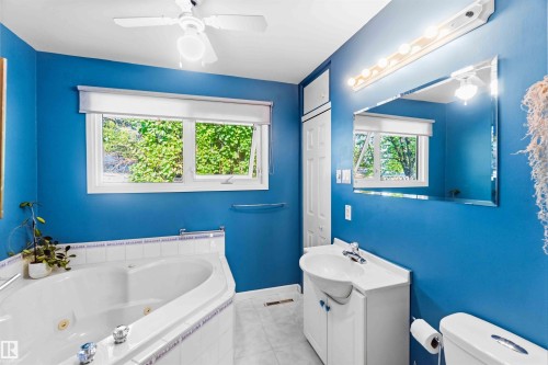 Bathroom featuring a white built-in jetted tub, a single vanity with a white basin sink, a mirror with strip lighting, and a window providing natural illumination - 5208 105 Street Nw, Edmonton, AB - Indoor Photo Showing Bathroom