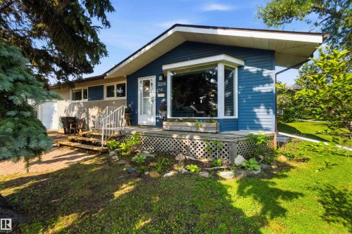 Residence featuring blue siding, a bay window, a front entry door with glass panels, a wooden porch with lattice detailing, and a paved walkway - 5208 105 Street Nw, Edmonton, AB - Outdoor With Deck Patio Veranda