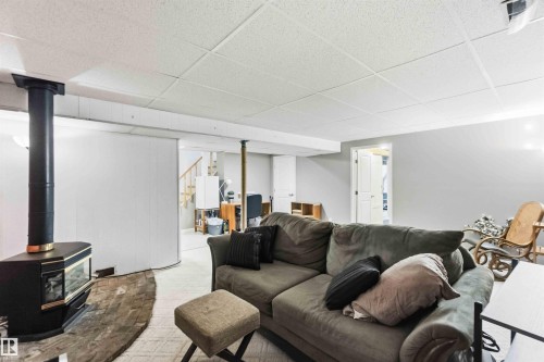 Finished basement space featuring a black freestanding stove with a glass door, a light-colored dropped ceiling, painted walls, and light-toned carpeting - 5208 105 Street Nw, Edmonton, AB - Indoor Photo Showing Living Room