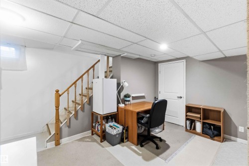 Finished basement area featuring a staircase with wood railing, recessed lighting, drop ceiling, and a white interior door - 5208 105 Street Nw, Edmonton, AB - Indoor Photo Showing Other Room
