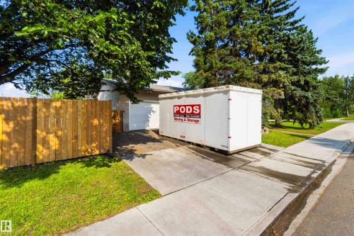 Concrete driveway with an attached garage, bordered by a wood privacy fence and mature trees - 5208 105 Street Nw, Edmonton, AB - Outdoor