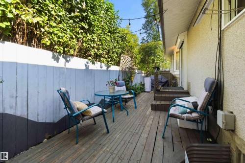 Wood deck patio with multi-level steps, bordered by a privacy fence with established green foliage, and featuring string lighting overhead - 5208 105 Street Nw, Edmonton, AB - Outdoor With Deck Patio Veranda With Exterior