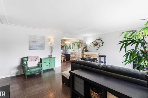 Spacious living area featuring dark wood-finish flooring, white walls, coved ceilings, and a wide arched entryway - 5208 105 Street Nw, Edmonton, AB - Indoor Photo Showing Living Room