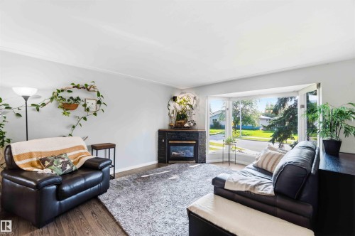 Open concept living space featuring a bay window, wood-finish flooring, and a stone-clad fireplace with a dark wood mantel - 5208 105 Street Nw, Edmonton, AB - Indoor Photo Showing Living Room With Fireplace