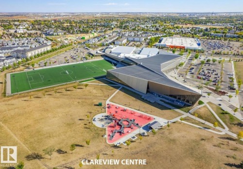 Modern architectural building with expansive parking, adjacent athletic field, and nearby residential structures - #1418 330 Clareview Station Dr Nw, Edmonton, AB - Outdoor With View