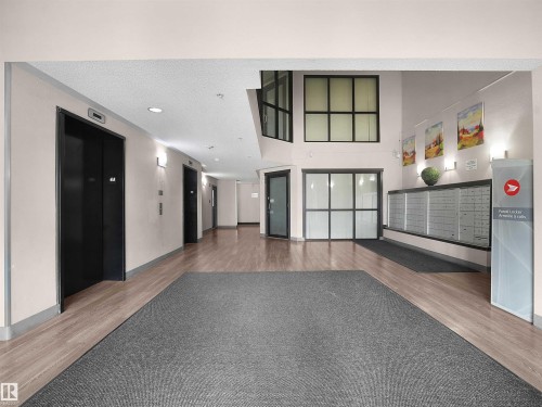 Wood-finish flooring with a large area rug, multiple elevators, and built-in mailboxes with parcel lockers - #1418 330 Clareview Station Dr Nw, Edmonton, AB - Indoor Photo Showing Other Room