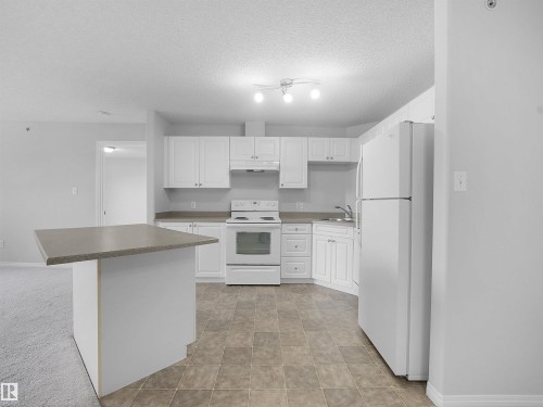 Full kitchen featuring white cabinetry, white appliances, durable tile flooring, and a peninsula with a contrasting countertop - #1418 330 Clareview Station Dr Nw, Edmonton, AB - Indoor Photo Showing Kitchen
