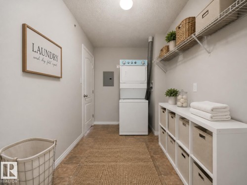 Brown-toned tile flooring, stacked washer and dryer, white wire shelving, white storage unit with cubbies, white door with dark hardware - #1418 330 Clareview Station Dr Nw, Edmonton, AB - Indoor Photo Showing Laundry Room