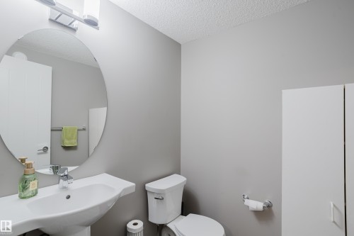 Pedestal sink with chrome faucet, oval mirror, and contemporary light fixture - #28 2215 24 St Nw, Edmonton, AB - Indoor Photo Showing Bathroom