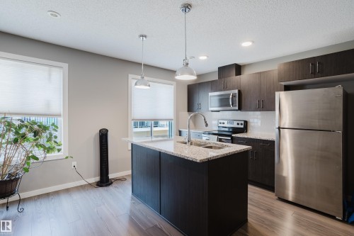 Kitchen featuring an island with a double basin sink, stainless steel appliances, dark wood-finish cabinetry, and wood-finish flooring - #28 2215 24 St Nw, Edmonton, AB - Indoor Photo Showing Kitchen With Double Sink With Upgraded Kitchen