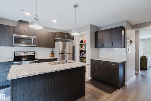 Modern kitchen featuring dark wood-finish cabinetry, light-toned granite countertops, and stainless steel appliances - #28 2215 24 St Nw, Edmonton, AB - Indoor Photo Showing Kitchen With Upgraded Kitchen