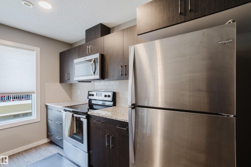 Kitchen featuring wood-finish cabinetry, light-toned countertops, and a subway tile backsplash - #28 2215 24 St Nw, Edmonton, AB - Indoor Photo Showing Kitchen