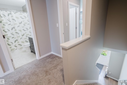 Carpeted hallway with a neutral color palette, white baseboards, and a partial wall overlooking a lower level - #28 2215 24 St Nw, Edmonton, AB - Indoor Photo Showing Other Room