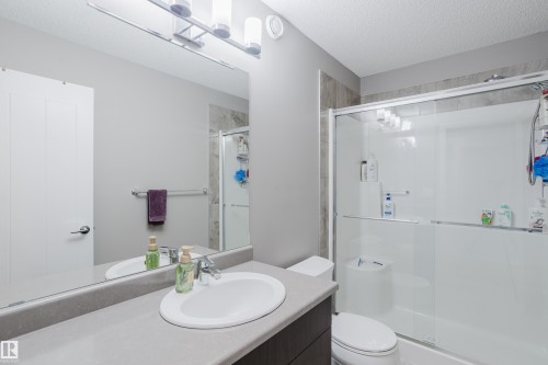 Bathroom featuring a vanity with an integrated sink, a large wall-mounted mirror, and a shower with sliding glass doors - #28 2215 24 St Nw, Edmonton, AB - Indoor Photo Showing Bathroom