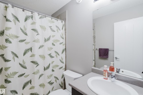 Bathroom featuring a white toilet, an integrated sink with a chrome faucet, and a large wall-mounted mirror - #28 2215 24 St Nw, Edmonton, AB - Indoor Photo Showing Bathroom