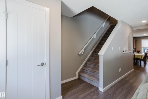 Hallway featuring wood-finish flooring, a carpeted staircase with white railing, a paneled interior door with lever hardware, neutral-toned walls, and recessed lighting - #28 2215 24 St Nw, Edmonton, AB - Indoor Photo Showing Other Room
