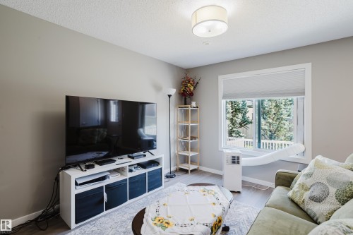 Living area featuring wood-finish flooring, light grey painted walls, a large window with roller blinds, and a flush-mount ceiling light fixture - #28 2215 24 St Nw, Edmonton, AB - Indoor Photo Showing Living Room