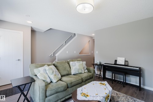 Spacious living area featuring neutral wall tones, recessed lighting, wood-finish flooring, a contemporary ceiling fixture, and a staircase with white railings - #28 2215 24 St Nw, Edmonton, AB - Indoor Photo Showing Other Room