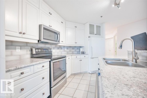 Kitchen featuring white cabinetry, light-colored countertops, stainless steel appliances, and a tiled backsplash - #108 12028 103 Av Nw, Edmonton, AB 