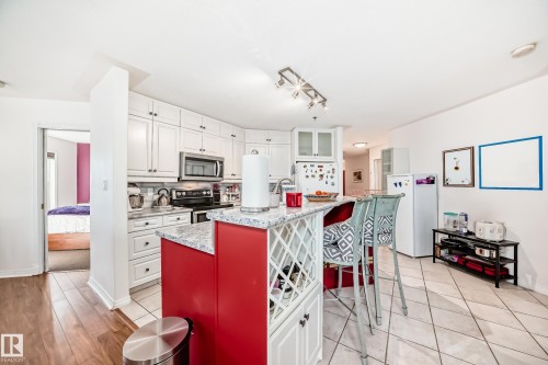 Kitchen featuring white cabinetry, stainless steel microwave, and a red kitchen island with a built-in wine rack - #108 12028 103 Av Nw, Edmonton, AB 