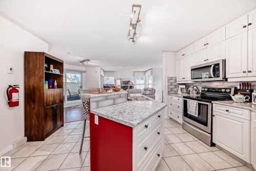 White shaker-style cabinetry with dark hardware, stainless steel appliances, granite countertops, and subway tile backsplash - #108 12028 103 Av Nw, Edmonton, AB 