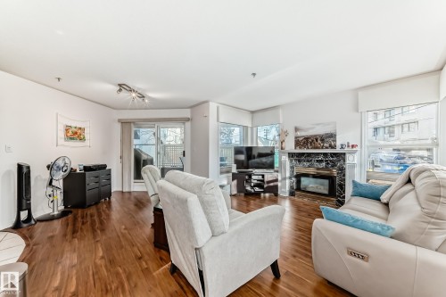 Wood-finish flooring throughout, complemented by a prominent fireplace with a dark stone surround and a built-in electric insert - #108 12028 103 Av Nw, Edmonton, AB 
