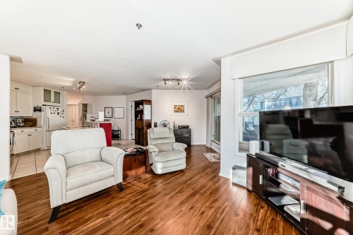 Wood-finish flooring, white kitchen cabinetry, recessed lighting, white tile flooring, and a large window - #108 12028 103 Av Nw, Edmonton, AB 