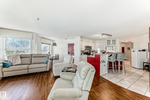 Open-concept living area featuring wood-finish flooring, white walls, and large windows - #108 12028 103 Av Nw, Edmonton, AB 
